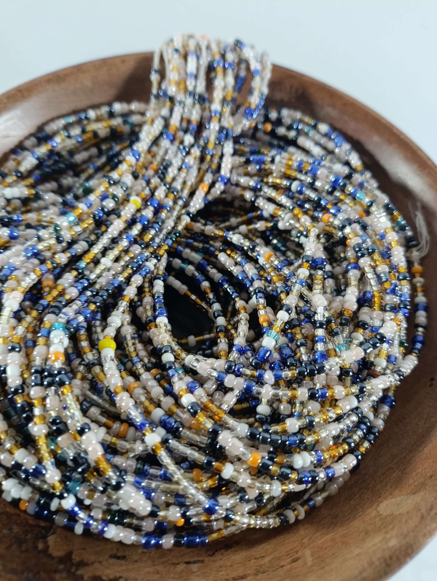 Perles Africaines 19 multicolores enfilées dans un bol en bois, idéales pour bijoux ethniques et accessoires artisanaux.